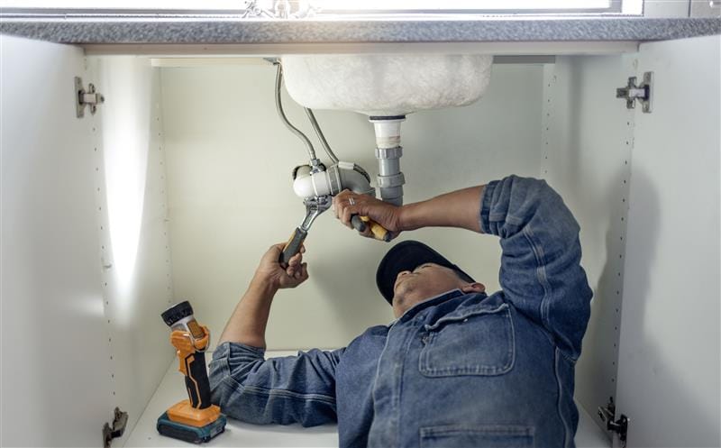 Plumber repairing pipes beneath a bathroom sink in Hollywood