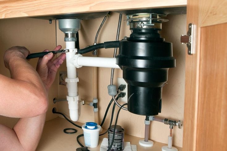 Plumber installing a garbage disposal beneath a kitchen sink in Hollywood