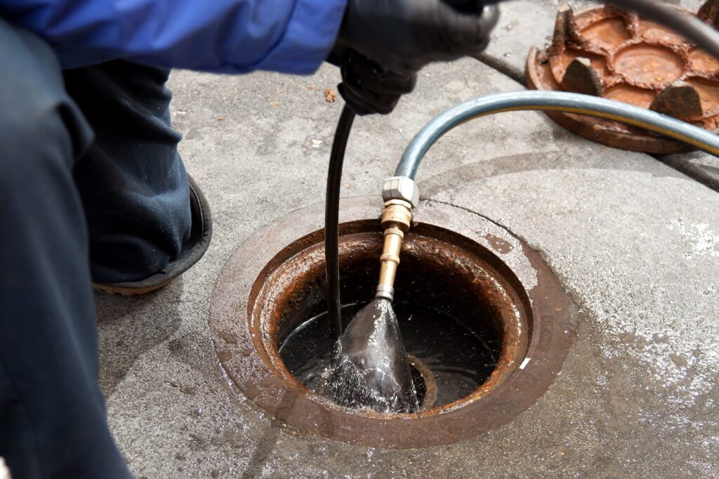 Plumber hydro jetting a sewer line through a manhole in Hollywood