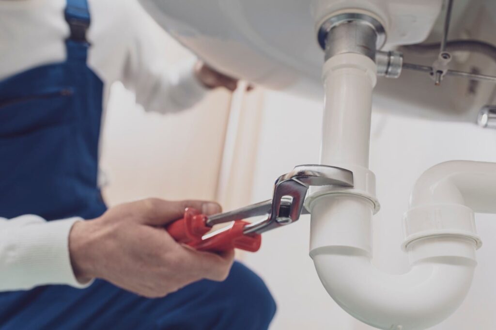 Plumber repairing a white drain pipe beneath a sink in Hollywood