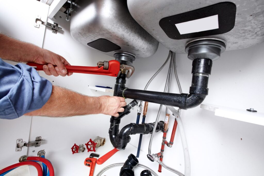 Plumber repairing drain pipes beneath a kitchen sink in Hollywood